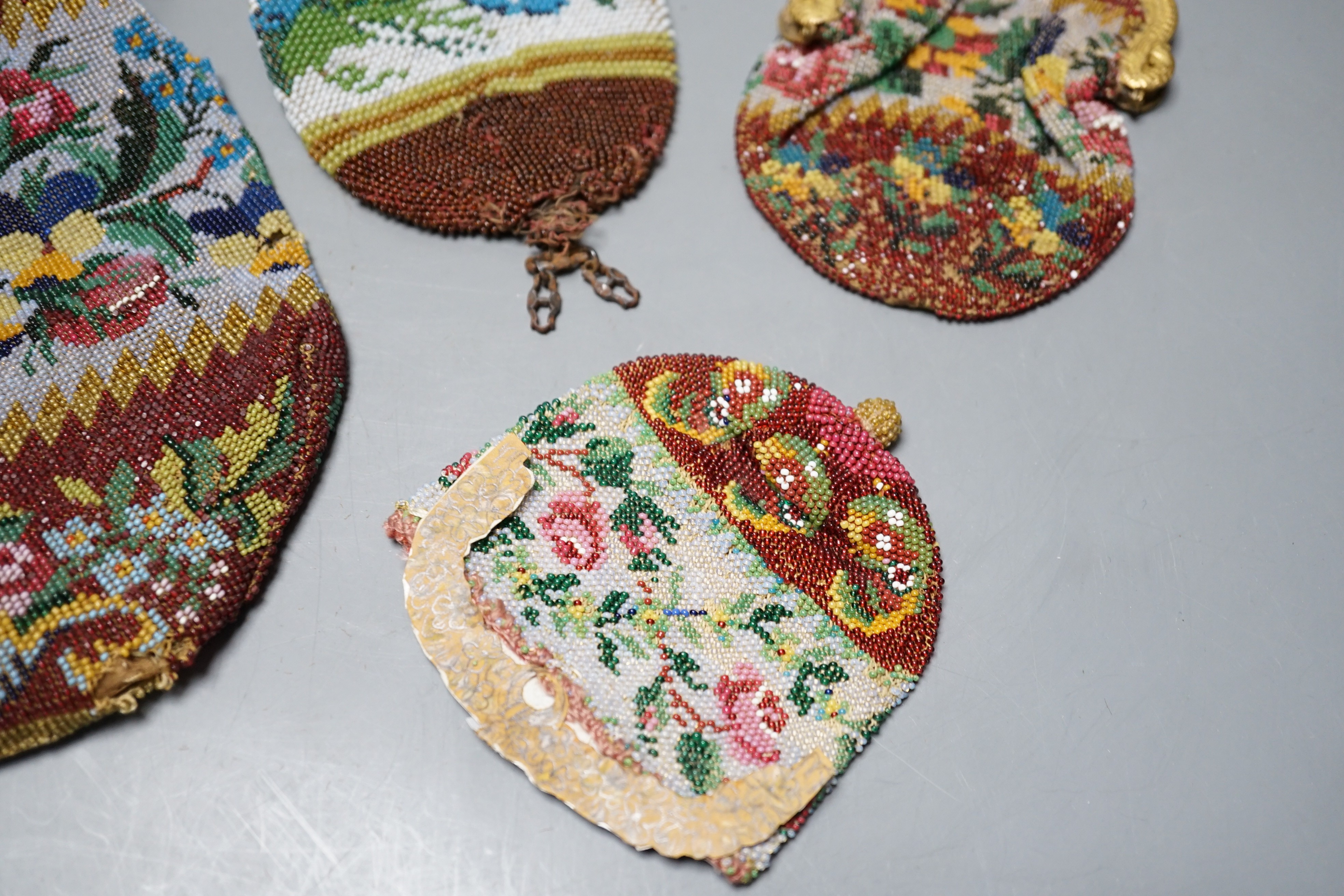 An early 19th century ornate gilt framed beaded bag with multi coloured floral design, together with three similar worked purses, gilt framed bag 20 cms high